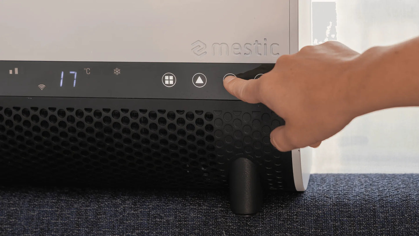 Hand pressing a button on a black air purifier with 'mestic' branding.