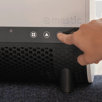 Hand pressing a button on a black air purifier with 'mestic' branding.