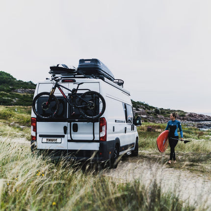Van with bike rack and person holding a surfboard in a natural setting